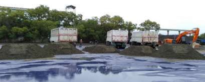 Dump trucks and excavator loading mineral sand from a tarped stockpile at the laydown yard